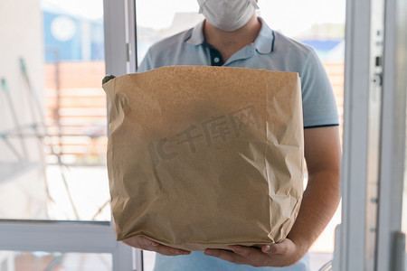 买送摄影照片_将戴着面罩的男子送到屋前，身穿蓝色制服处理袋的食物交给顾客。