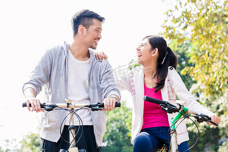年轻的亚洲夫妇骑自行车时一起笑