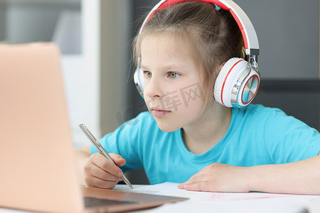 一个戴耳机的女孩专注地看着笔记本电脑