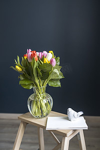 粉色台阶摄影照片_一束多色郁金香放在高脚椅上的透明花瓶中，深蓝色背景上有台阶。
