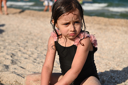 头像湿头发和泳装的可爱心烦意乱的女婴的肖像，坐在大海背景的沙滩上。