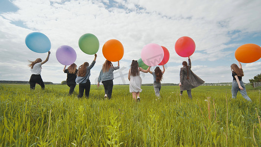女朋友们拿着大气球和彩色气球走过田野。