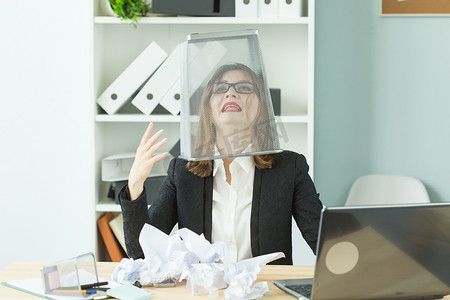 压力、办公室、人的观念 — 坐在办公室桌子旁工作量很大的女工把一个垃圾箱放在头上尖叫
