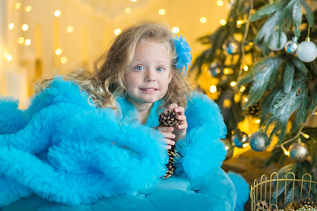 年轻漂亮的女孩穿着蓝色白色优雅的晚礼服，坐在圣诞树附近的地板上，在除夕夜送礼物。