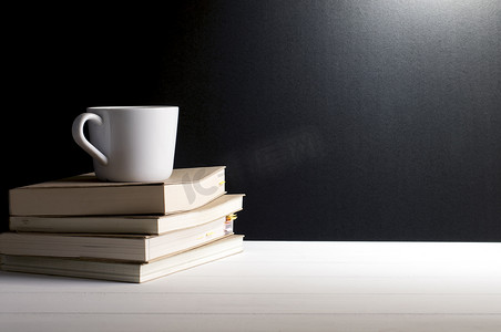 字体摄影照片_静物画-一杯咖啡放在白色木桌上的旧书上，以垃圾黑色背景的字体。