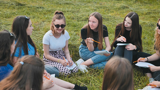 一群女学生在草地上围坐成一圈，拿着笔记本集体作业。