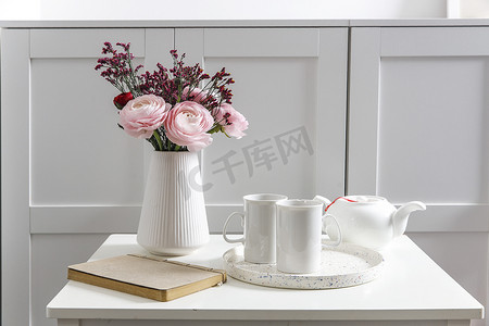 五斗柜前的白色桌子上放着一束粉红色的波斯毛茛。