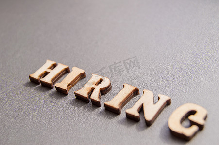 广告招聘用“HIRING”一词表示，由灰色背景上的木制字母组成。