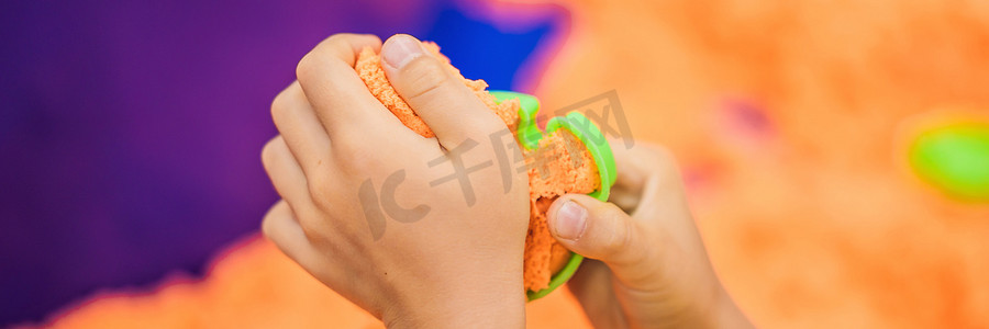 游戏banner摄影照片_男孩的手在玩橙色动感沙 BANNER, LONG FORMAT