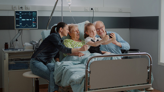 住院探视摄影照片_孩子在探视时与生病的病人和家人在智能手机上自拍