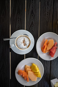 在黑桌上享用美味的拿铁咖啡和切片水果早餐