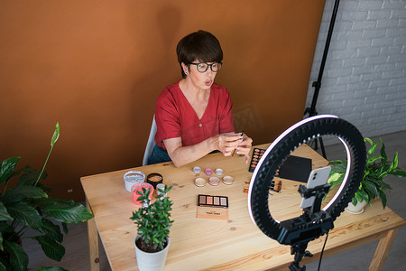 中年妇女在录制视频时用眼影、腮红调色板和刷子谈论化妆品。