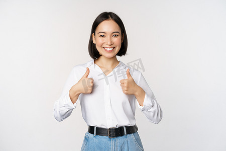 美丽的亚洲成年女性竖起大拇指、穿着正式办公室、大学服装、推荐公司、站在白色背景上的形象