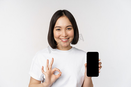 微笑的亚洲女性表现得很好，手机屏幕，推荐智能手机应用，站在白色背景上