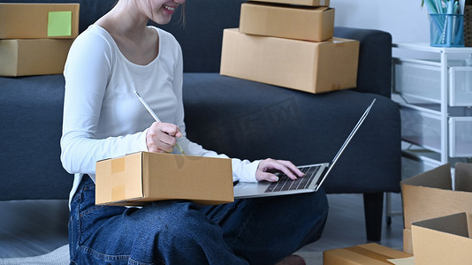 启动小企业企业家在笔记本电脑上确认客户的订单并准备包裹箱以供交付