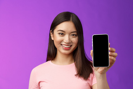 程序小摄影照片_特写迷人宜人的女店员展示新手机应用程序，手持智能手机显示电话屏幕，介绍展示应用程序，站立紫色背景高兴