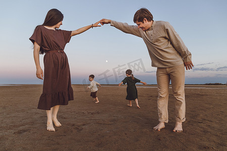 有两个小孩的年轻父母晚上在沙滩上玩耍和跳舞