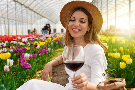春天，轻松美丽的女人在郁金香之间享用一杯红酒