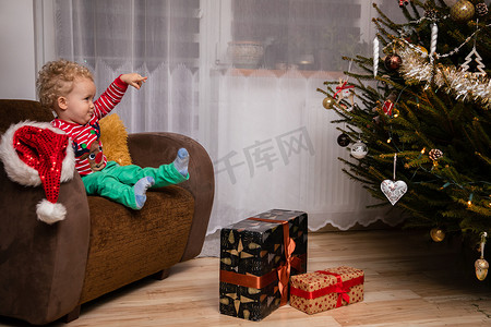 一个微笑的两岁孩子用手指着一棵圣诞树。