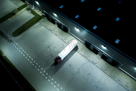 夜间现代物流中心、白色货车和拖车站在坡道上。