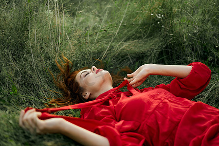 清新空气摄影照片_穿着红色连衣裙的漂亮女人躺在田野自然清新空气的草地上