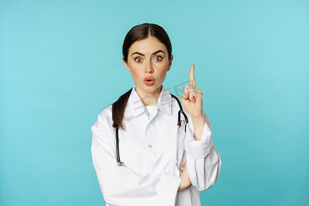 年轻医生，穿白大褂的女医生举起手指，指着，暗示 smth，有解决方案，启示，站在绿松石背景上