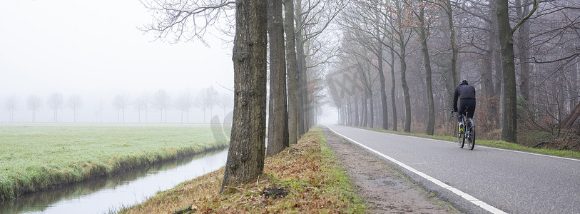 荷兰乌得勒支附近雾蒙蒙的冬日早晨，男子在乡间小路上骑自行车