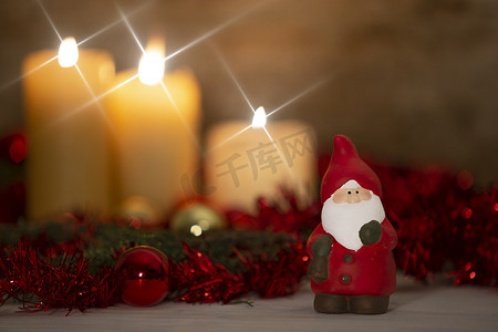 圣诞节概念的温暖：前景中的圣诞老人雕像，乡村环境，三支蜡烛点燃，散景效果，金色和红色明亮的小玩意，跨屏星形效果