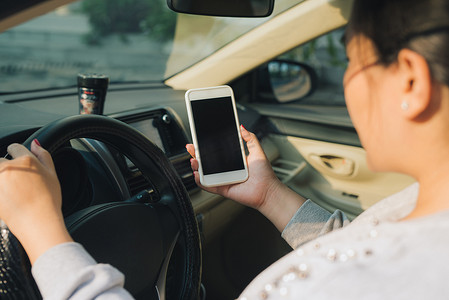 汽车智能驾驶摄影照片_在汽车中使用带空白屏幕的智能手机的女司机的样机图像。