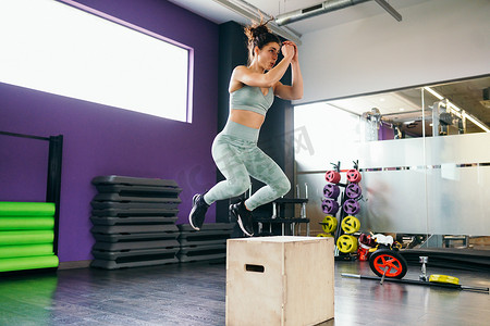 日常装备摄影照片_作为日常锻炼的一部分，健身女人跳上一个盒子。
