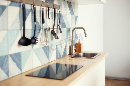 瓷砖摄影照片_蓝色几何图案瓷砖墙上的厨房铲子放在栏杆上