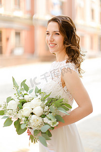 快乐的欧洲新娘拿着一束鲜花，穿着白色的裙子。