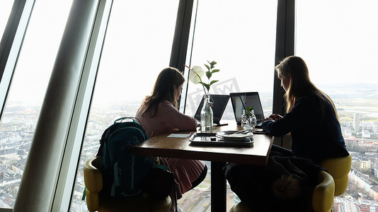 德国杜塞尔多夫 — 2020年2月24日：在一家俯瞰城市的现代咖啡馆内，两名女商人坐在窗边，拿着笔记本电脑。