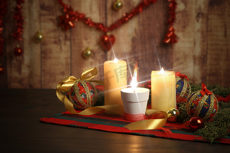 圣诞桌布上点着大火焰的蜡烛，周围有松树枝、剪纸小饰物、点燃的蜡烛和悬挂在木制背景上的圣诞装饰，具有散景效果