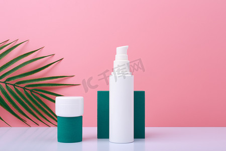 两个几何形状的奶油罐，用于在带棕榈叶的粉红色背景的白桌上展示产品