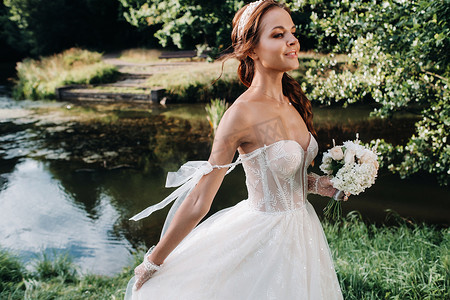 自然公园里一位穿着白色连衣裙、戴着花束的优雅新娘的肖像。穿着婚纱、戴着手套和花束的模特。白俄罗斯