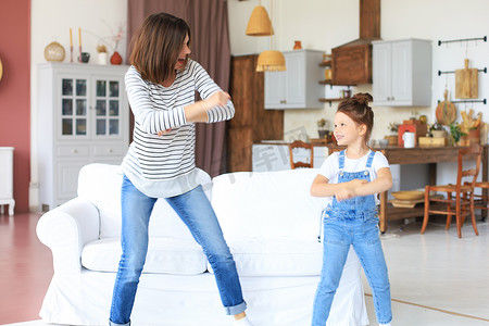 儿童歌曲大赛摄影照片_快乐的母亲带着小女儿在家里的客厅里随着最喜欢的歌曲跳舞。
