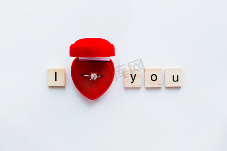 白色背景与木字我爱你和红色礼品盒中的钻石订婚戒指。