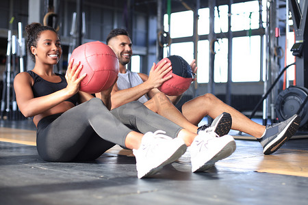美丽的年轻运动夫妇正在健身房锻炼药球。