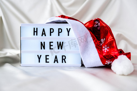 灯箱与文本新年快乐与圣诞老人帽子在丝绸织物背景。