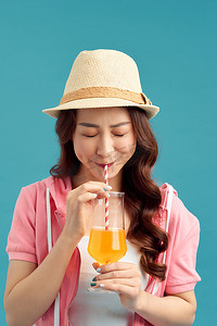 在蓝色背景下喝果汁的年轻亚洲美女。