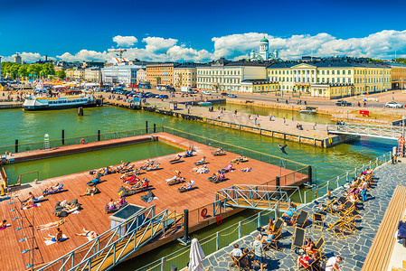 赫尔辛基 — 2019年6月，芬兰：赫尔辛基港的城市景观，人们在码头上晒日光浴