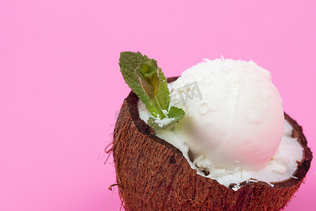 新鲜椰子半块的香草冰淇淋球，装饰着粉红色背景的薄荷叶