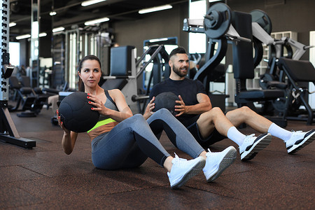 坐在健身房地板上的运动年轻人在腹部锻炼期间与药球一起锻炼