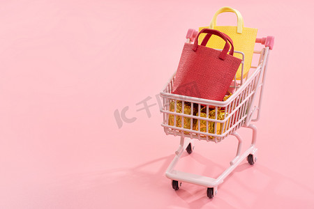 年度销售购物季概念 — 迷你红色购物车手推车，里面装满纸袋礼品，以淡粉色背景隔开，空白复制空间，特写