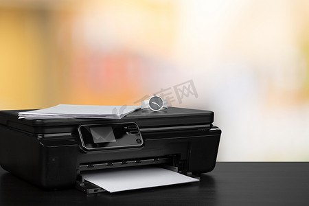 背景模糊的黑色办公桌上的紧凑型激光打印机
