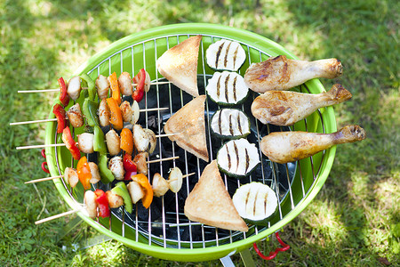 在野餐或夏季露营旅行期间，便携式烧烤站在绿色草坪上，有复制空间