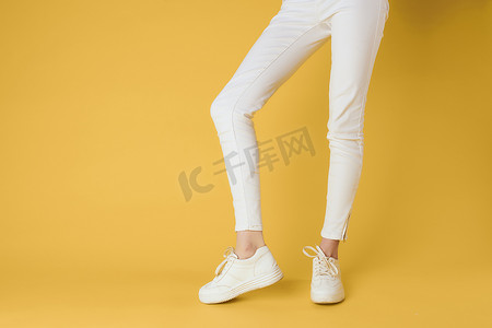 女性腿白色裤子运动鞋时尚服装奢华街头风格黄色背景