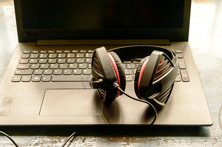 噪摄影照片_便携式耳罩式双耳 USB 耳机，带麦克风降噪和超声波音量调节器耳机，适用于计算机、Skype，在早晨阳光下放置在笔记本电脑上。