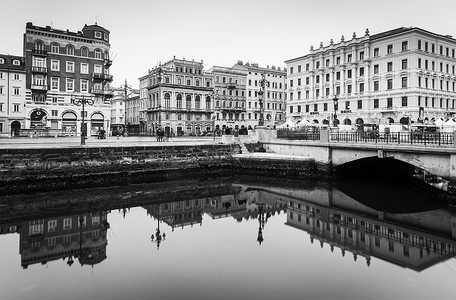 的里雅斯特 — 2016 年 12 月，意大利：古老的历史建筑镜面反射在水中，里雅斯特市中心的大运河，黑白城市景观
